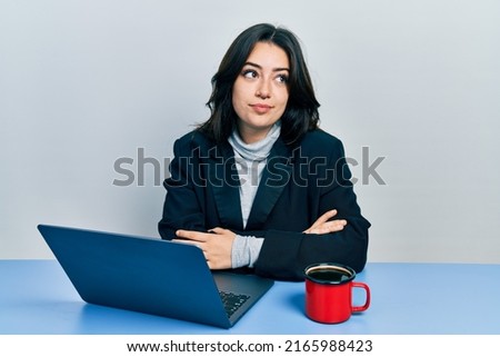 Beautiful hispanic business woman with arms crossed gesture at the office smiling looking to the side and staring away thinking. 