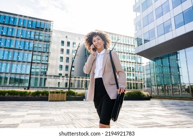 Beautiful Hispanic Businesswoman With Elegant Suit Walking In The Business Centre- Adult Female With Business Suit And Holding Mobile Phone Portrait Outdoors