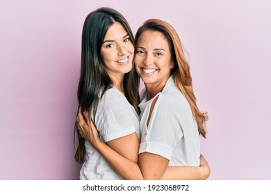 Schöne hispanische Mutter und Tochter lächeln glücklich umarmt auf isoliertem rosa Hintergrund.