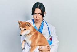 Beautiful Hispanic Veterinarian Woman Holding Dog Skeptic And Nervous, Frowning Upset Because Of Problem. Negative Person. 