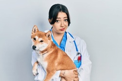 Beautiful Hispanic Veterinarian Woman Holding Dog Skeptic And Nervous, Frowning Upset Because Of Problem. Negative Person. 
