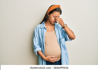 Beautiful Hispanic Woman Expecting A Baby, Touching Pregnant Belly Tired Rubbing Nose And Eyes Feeling Fatigue And Headache. Stress And Frustration Concept. 