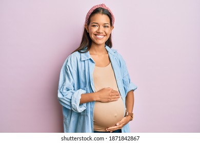 Beautiful Hispanic Woman Expecting A Baby, Touching Pregnant Belly Smiling With A Happy And Cool Smile On Face. Showing Teeth. 