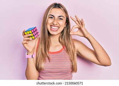 Beautiful Hispanic Woman Holding Colorful Puzzle Cube Intelligence Game Doing Ok Sign With Fingers, Smiling Friendly Gesturing Excellent Symbol 