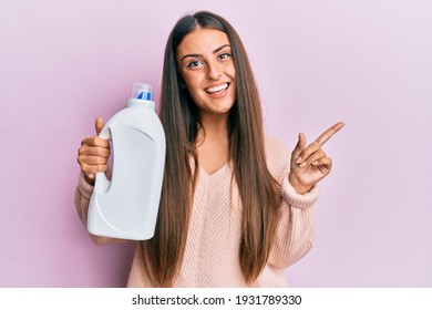 Beautiful Hispanic Woman Holding Laundry Detergent Bottle Smiling Happy Pointing With Hand And Finger To The Side 