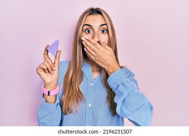 Beautiful Hispanic Woman Holding Makeup Sponge Covering Mouth With Hand, Shocked And Afraid For Mistake. Surprised Expression 