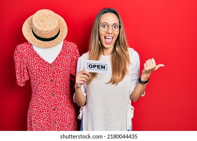 Beautiful hispanic woman holding open shopping business banner pointing thumb up to the side smiling happy with open mouth 