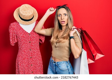 Beautiful hispanic woman holding shopping bags by retail manikin in shock face, looking skeptical and sarcastic, surprised with open mouth 