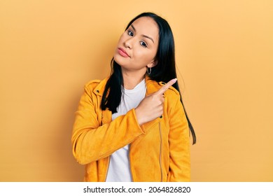 Beautiful hispanic woman with nose piercing wearing yellow leather jacket pointing with hand finger to the side showing advertisement, serious and calm face 