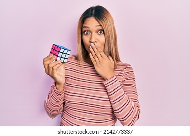 Beautiful Hispanic Woman Playing Colorful Puzzle Cube Intelligence Game Covering Mouth With Hand, Shocked And Afraid For Mistake. Surprised Expression 