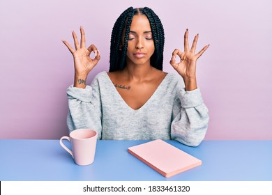 Beautiful Hispanic Woman Reading A Book And Drinking A Coffee Relax And Smiling With Eyes Closed Doing Meditation Gesture With Fingers. Yoga Concept. 