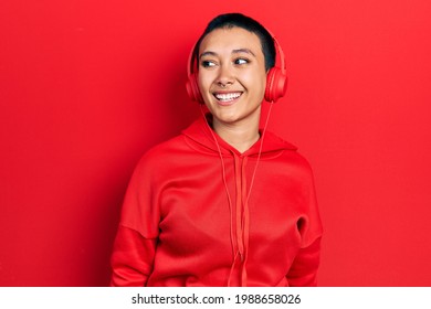 Beautiful hispanic woman with short hair listening to music using headphones looking away to side with smile on face, natural expression. laughing confident.  - Shutterstock ID 1988658026
