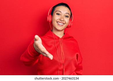 Beautiful hispanic woman with short hair listening to music using headphones smiling friendly offering handshake as greeting and welcoming. successful business.  - Shutterstock ID 2027463134