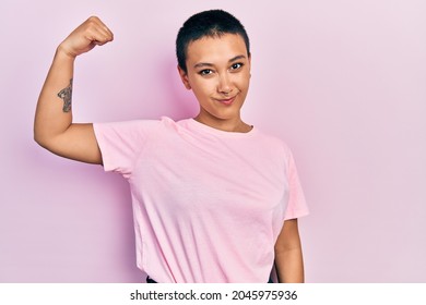 Beautiful Hispanic Woman With Short Hair Wearing Casual Pink T Shirt Strong Person Showing Arm Muscle, Confident And Proud Of Power 