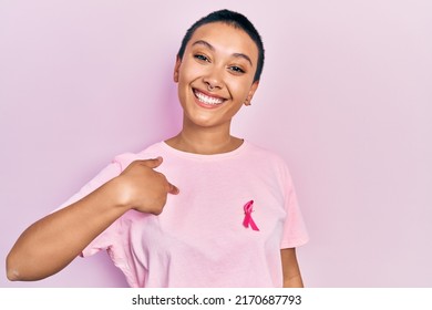 Beautiful hispanic woman with short hair wearing pink cancer ribbon on shirt pointing finger to one self smiling happy and proud  - Powered by Shutterstock