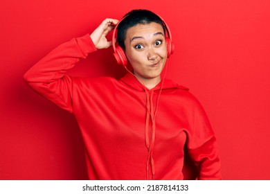 Beautiful Hispanic Woman With Short Hair Listening To Music Using Headphones Confuse And Wonder About Question. Uncertain With Doubt, Thinking With Hand On Head. Pensive Concept. 