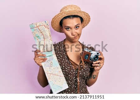 Beautiful hispanic woman with short hair holding city map and vintage camera skeptic and nervous, frowning upset because of problem. negative person. 