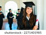 Beautiful hispanic woman smiling making eye contact after getting her university diploma at a graduation ceremony on campus