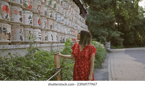 Beautiful hispanic woman smiling, standing by shake barrels at meiji temple while embracing japanese culture, all while donning glasses