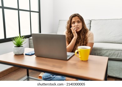 Beautiful Hispanic Woman Using Computer Laptop At Home Looking Stressed And Nervous With Hands On Mouth Biting Nails. Anxiety Problem. 