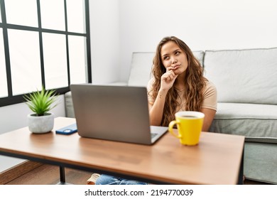 Beautiful Hispanic Woman Using Computer Laptop At Home Serious Face Thinking About Question With Hand On Chin, Thoughtful About Confusing Idea 