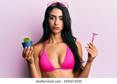 Beautiful Hispanic Woman Wearing Bikini Holding Cactus And Razor Skeptic And Nervous, Frowning Upset Because Of Problem. Negative Person. 