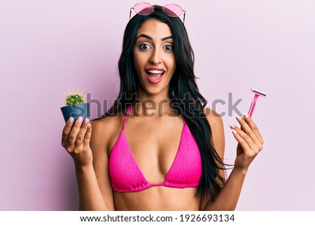 Beautiful hispanic woman wearing bikini holding cactus and razor celebrating crazy and amazed for success with open eyes screaming excited. 