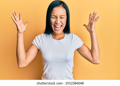 Beautiful hispanic woman wearing casual white tshirt celebrating mad and crazy for success with arms raised and closed eyes screaming excited. winner concept  - Shutterstock ID 1912384048