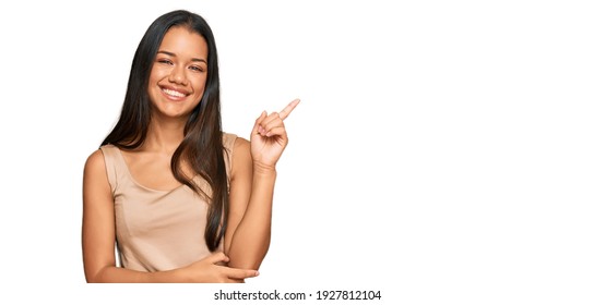 Beautiful Hispanic Woman Wearing Casual Clothes With A Big Smile On Face, Pointing With Hand And Finger To The Side Looking At The Camera. 