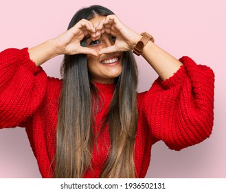 Beautiful hispanic woman wearing casual clothes doing heart shape with hand and fingers smiling looking through sign 
