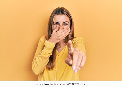 Beautiful Hispanic Woman Wearing Casual Yellow Sweater Laughing At You, Pointing Finger To The Camera With Hand Over Mouth, Shame Expression 