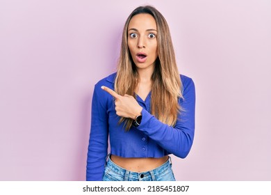 Beautiful hispanic woman wearing casual blue shirt surprised pointing with finger to the side, open mouth amazed expression. 