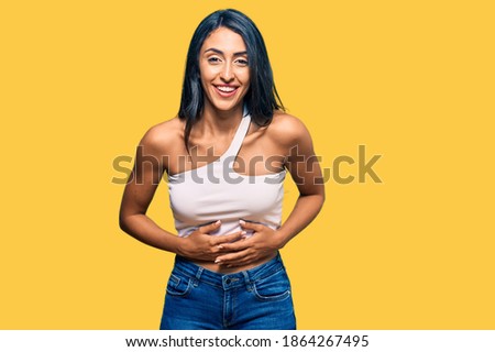 Beautiful hispanic woman wearing casual clothes smiling and laughing hard out loud because funny crazy joke with hands on body. 