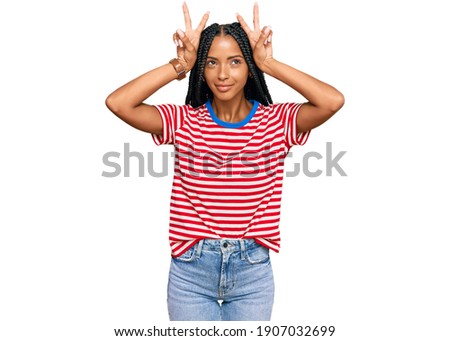 Beautiful hispanic woman wearing casual clothes doing funny gesture with finger over head as bull horns 