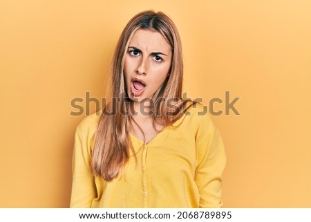 Beautiful hispanic woman wearing casual yellow sweater in shock face, looking skeptical and sarcastic, surprised with open mouth 