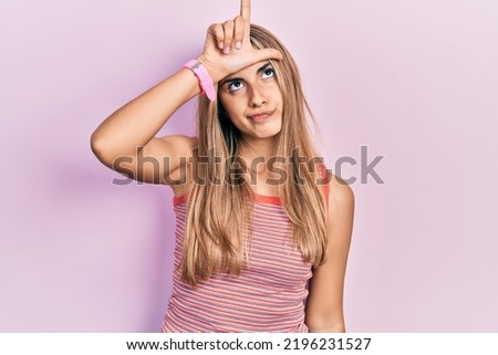 Beautiful hispanic woman wearing casual summer t shirt making fun of people with fingers on forehead doing loser gesture mocking and insulting. 