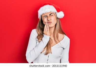 Beautiful hispanic woman wearing christmas hat touching mouth with hand with painful expression because of toothache or dental illness on teeth. dentist 