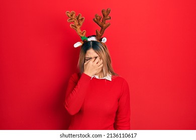 Beautiful Hispanic Woman Wearing Deer Christmas Hat And Red Nose Tired Rubbing Nose And Eyes Feeling Fatigue And Headache. Stress And Frustration Concept. 