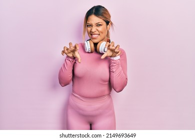 Beautiful Hispanic Woman Wearing Gym Clothes And Using Headphones Smiling Funny Doing Claw Gesture As Cat, Aggressive And Sexy Expression 