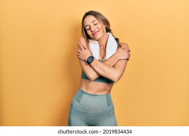 Beautiful hispanic woman wearing sportswear and towel hugging oneself happy and positive, smiling confident. self love and self care 