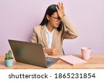 Beautiful hispanic woman working at the office wearing glasses surprised with hand on head for mistake, remember error. forgot, bad memory concept. 