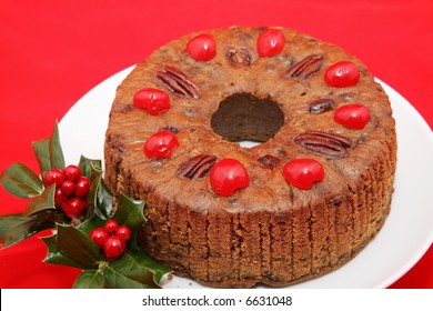 A Beautiful Holiday Fruitcake Garnished With Holly On A Bright Red Background.