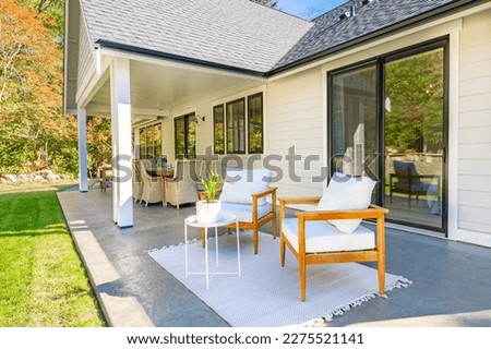 beautiful home exterior and patio on a bright colorful summer day with white painted house green grass lush landscape wicker deck furniture armchairs and blue sky