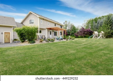 Beautiful House Backyard With Well Kept Lawn, Patio Area And Playground At The Background