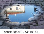 A beautiful house is vividly reflected in a calm puddle resting on a weathered brick sidewalk, creating an intriguing visual effect