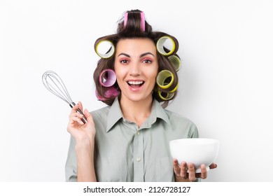 Beautiful Housewife. Young Cheerful Woman With Hair Curlers, Bright Make-up, A White Cup And A Whisk In Her Hands, On A White Background. Thinking About The Recipe For Dinner.