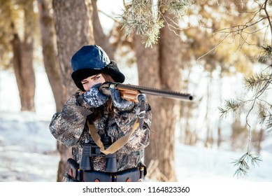 A beautiful hunter in a camouflage suit walks through the woods with weapons, preparing to hunt.
