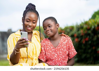 beautiful image of African lady holding smart phone and a kid besides her- seated black people enjoying social media surf - Powered by Shutterstock