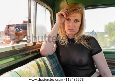 A beautiful implied blonde model posing in a auto salvage yard.