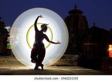 Beautiful Indian classical Odissi dancer dance recital against the backdrop of at Mukteshvara Temple sculpture light painting behind.